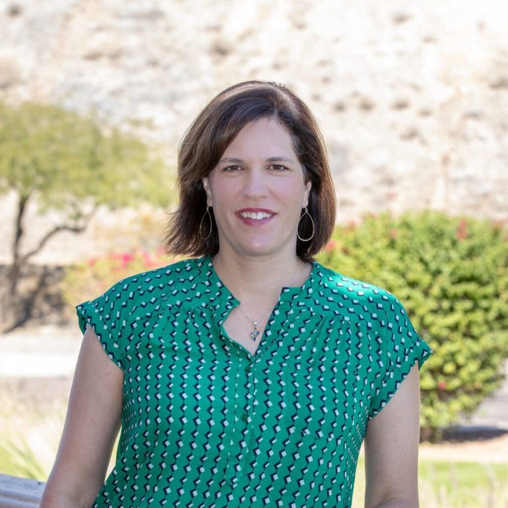 A woman in green shirt standing next to trees.