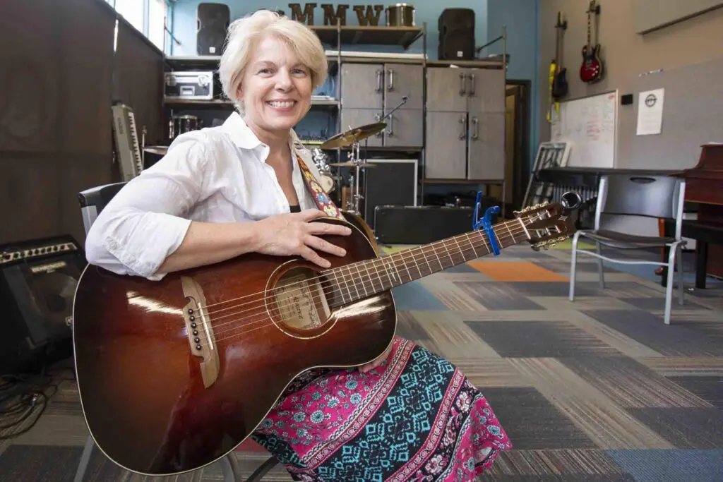 A woman sitting on the floor holding an acoustic guitar.