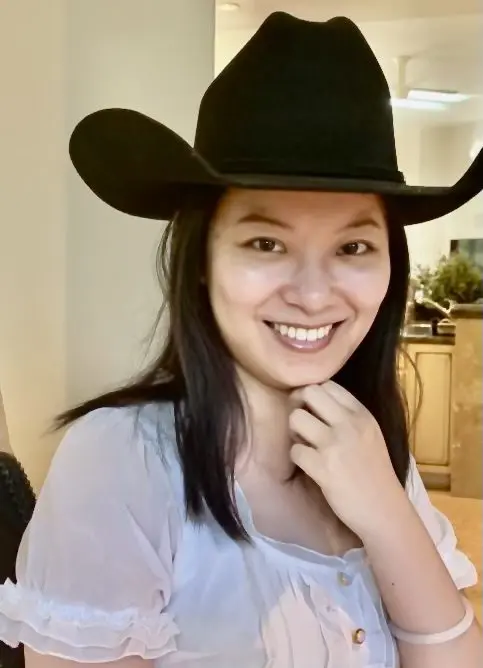 A woman wearing a black cowboy hat and smiling.