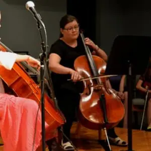 A woman playing the cello in front of other people.