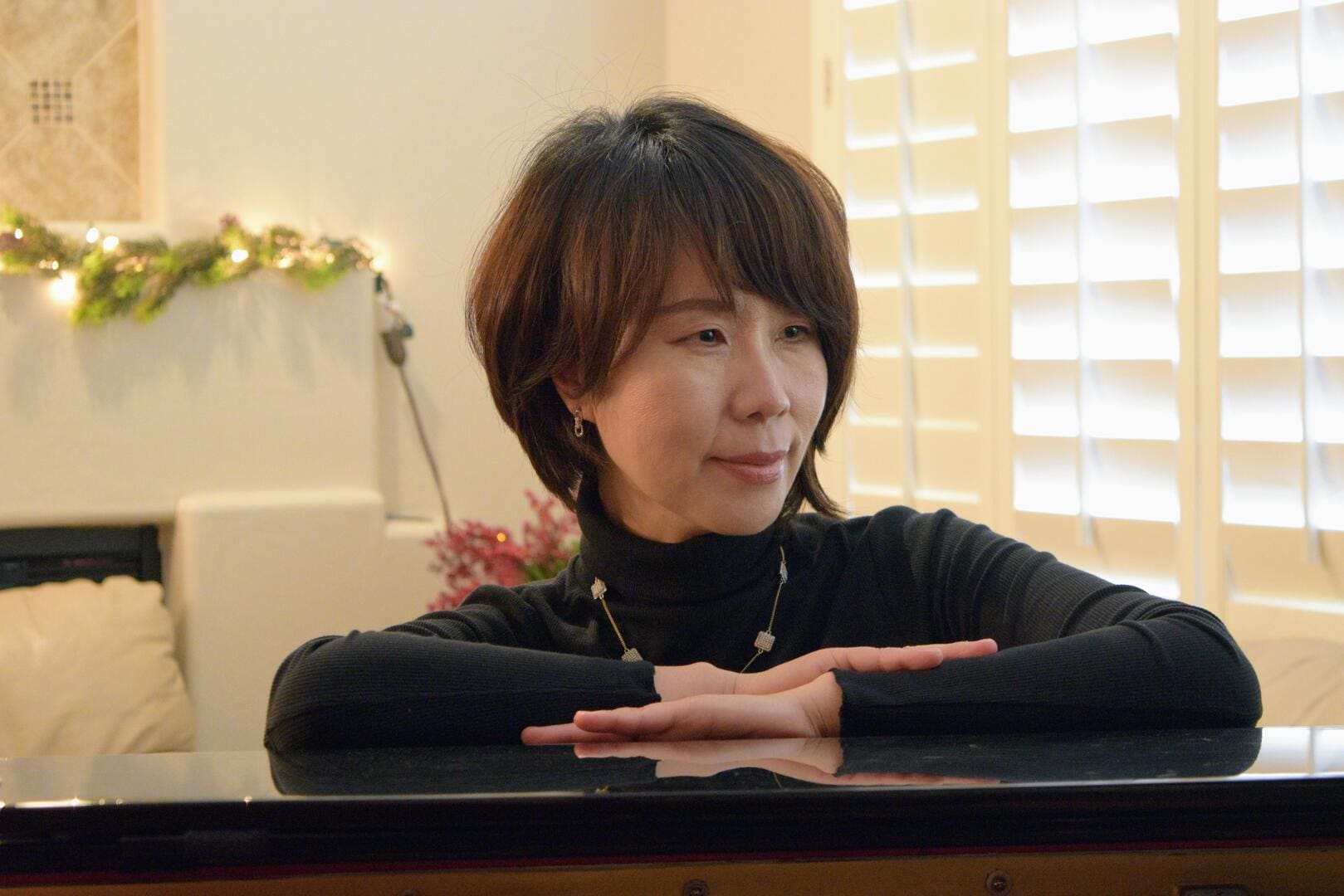 A woman sitting at the piano with her hands crossed.