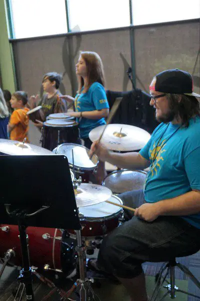 A man playing drums with other people behind him.