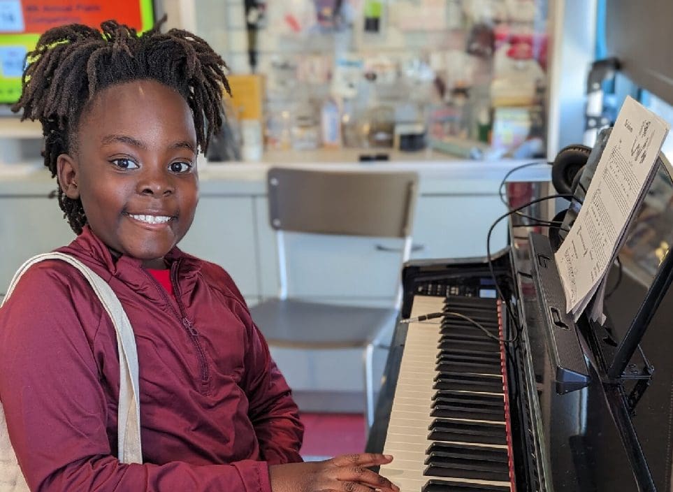 A young person sitting at the piano smiling.