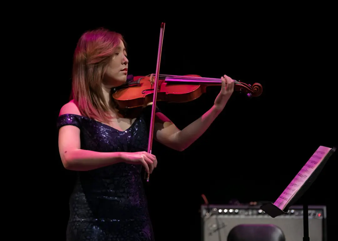 A woman playing the violin on stage with other people.