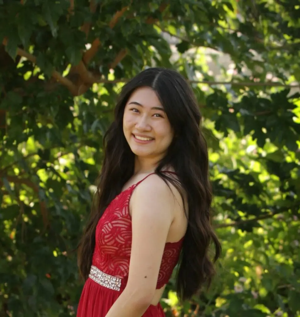 A woman in red dress standing next to tree.