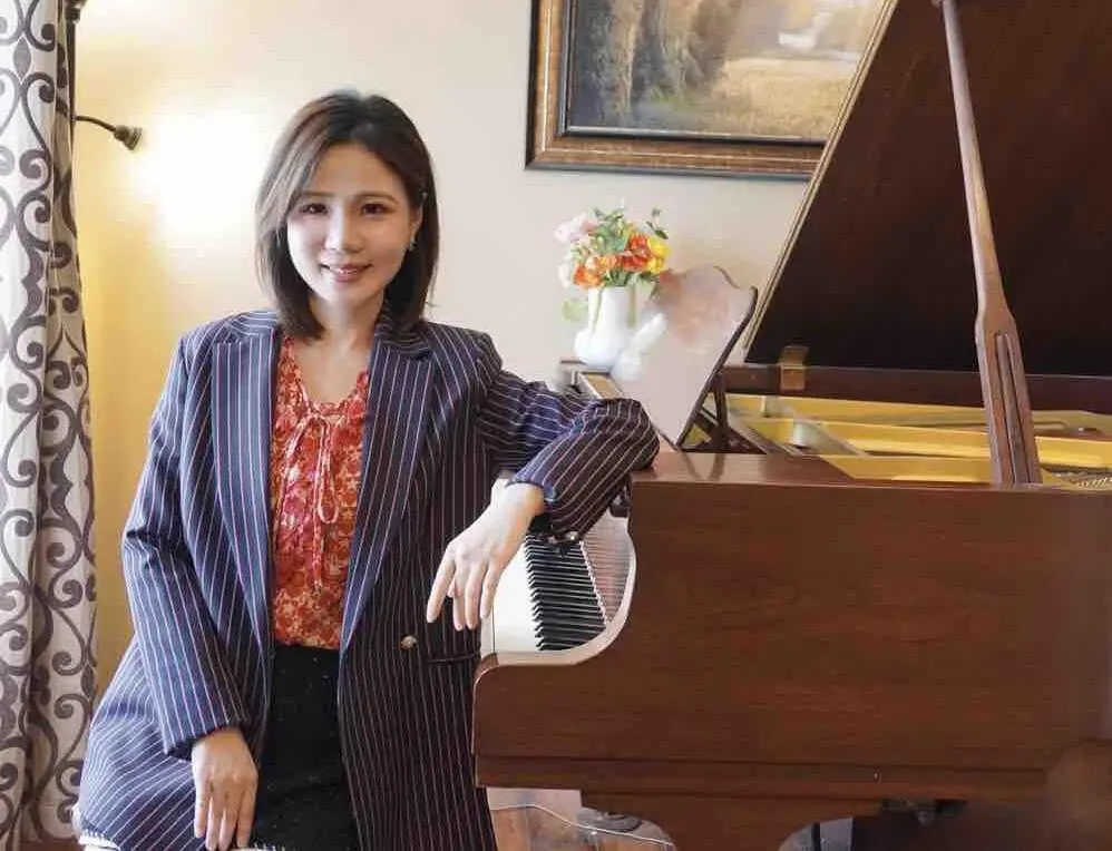 A woman in a suit sitting next to a piano.