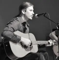 A man playing an acoustic guitar while holding a microphone.