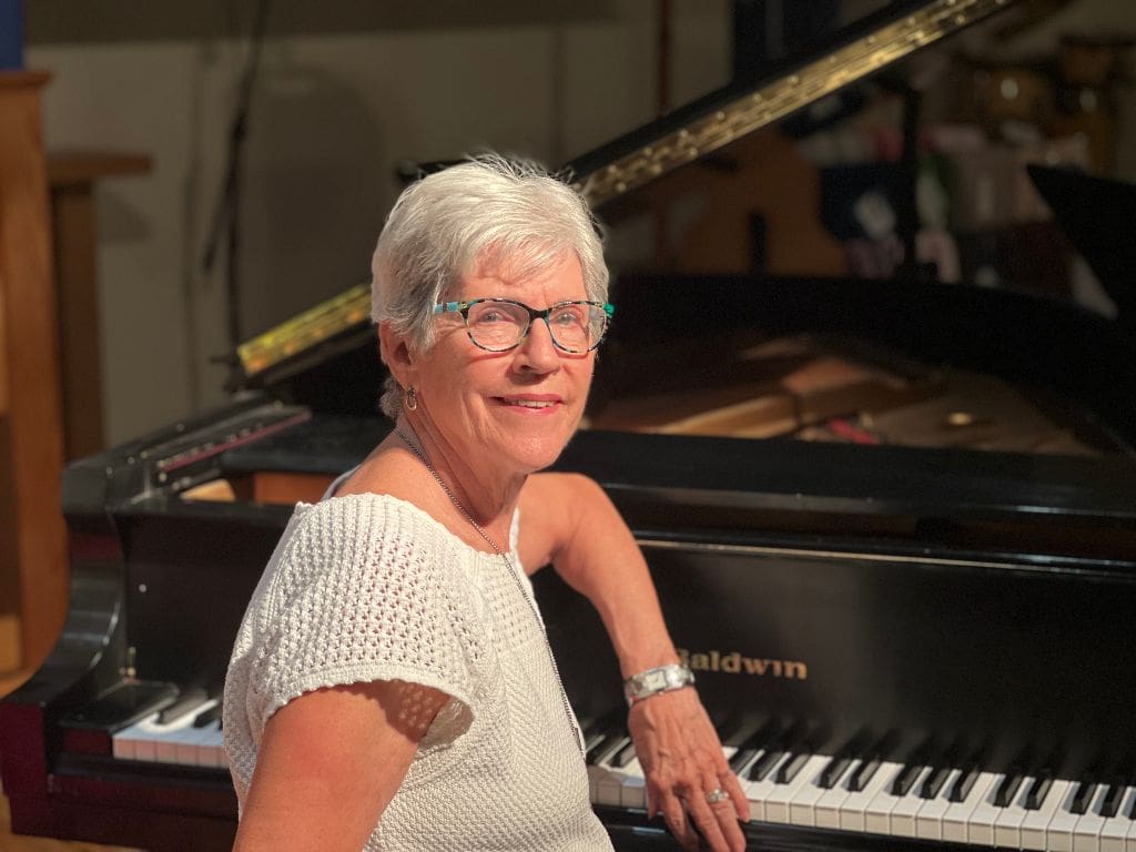 A woman standing next to a piano in front of a black grand piano.