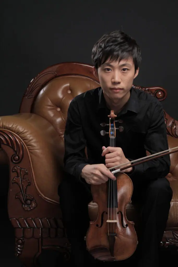 A man sitting in an arm chair holding a violin.