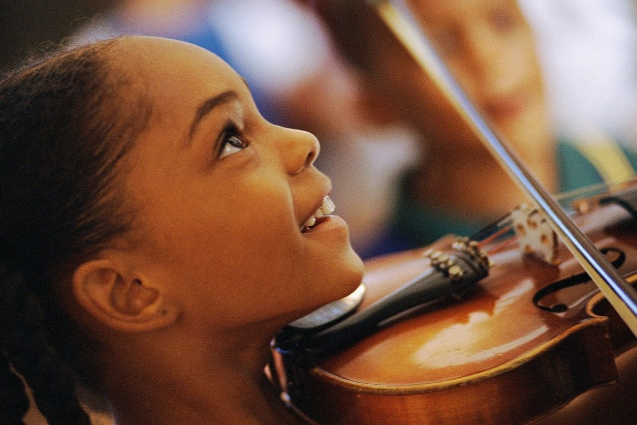 A young girl is playing the violin in an orchestra.