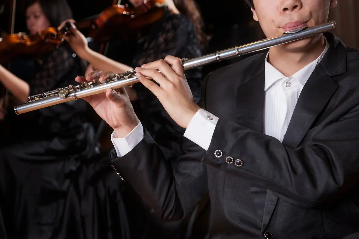 A man in black suit playing flute with other people.