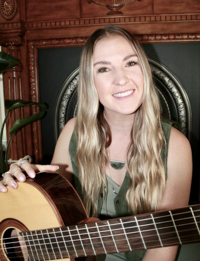 A woman holding a guitar in front of a wall.