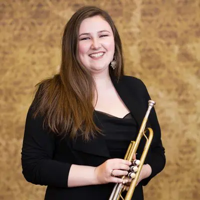 A woman holding a trumpet in front of a brown wall.