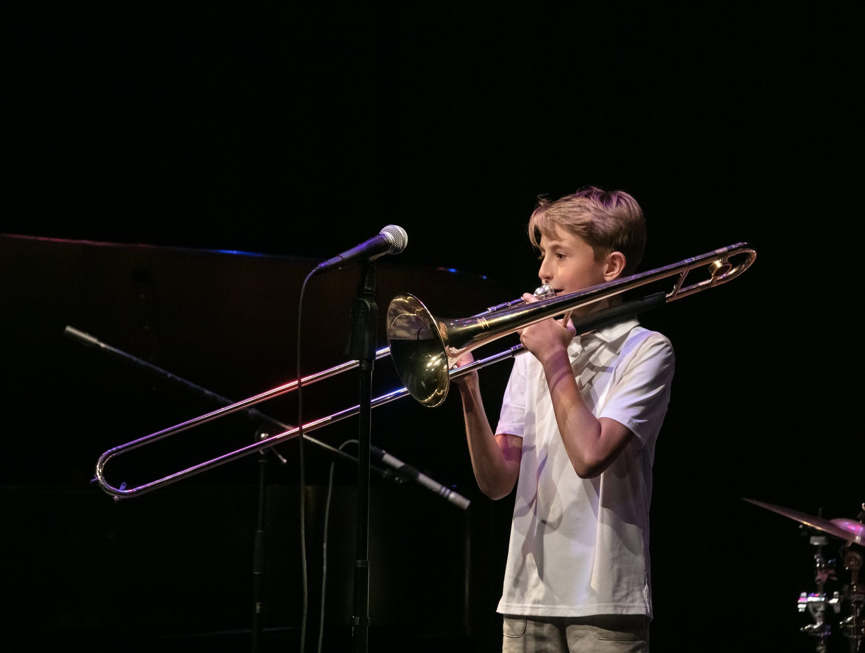 A boy playing trombone on stage with microphones.