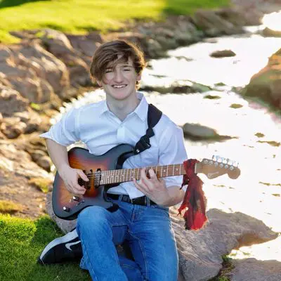 A man sitting on the grass holding a guitar.