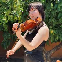 A woman playing the violin in front of trees.