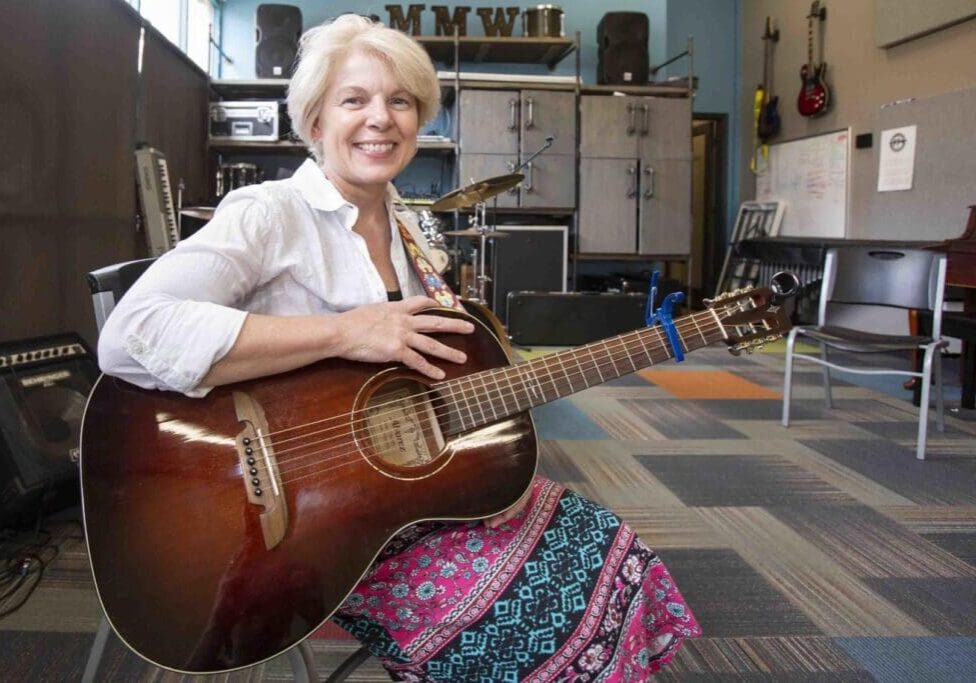 A woman sitting on the floor holding an acoustic guitar.