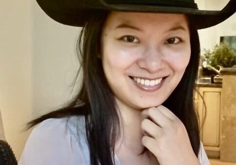 A woman wearing a black cowboy hat and smiling.