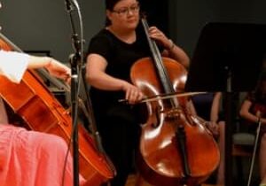 A woman playing the cello in front of other people.