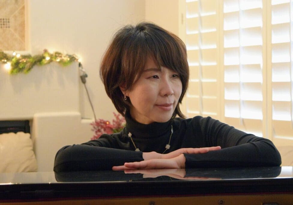 A woman sitting at the piano with her hands crossed.