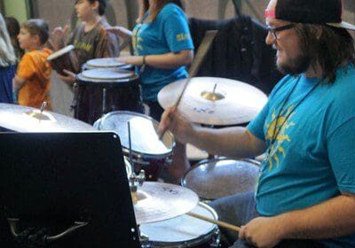 A man playing drums with other people behind him.