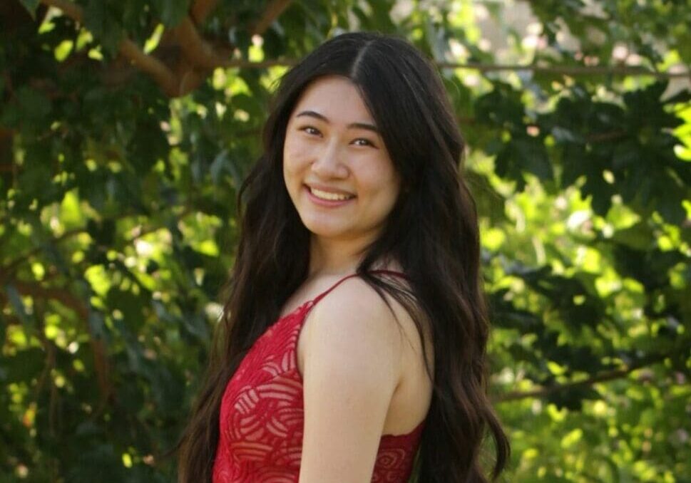 A woman in red dress standing next to tree.