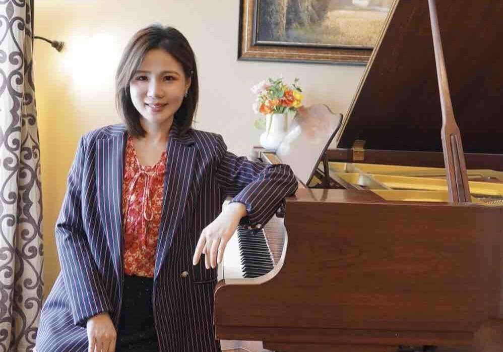 A woman in a suit sitting next to a piano.