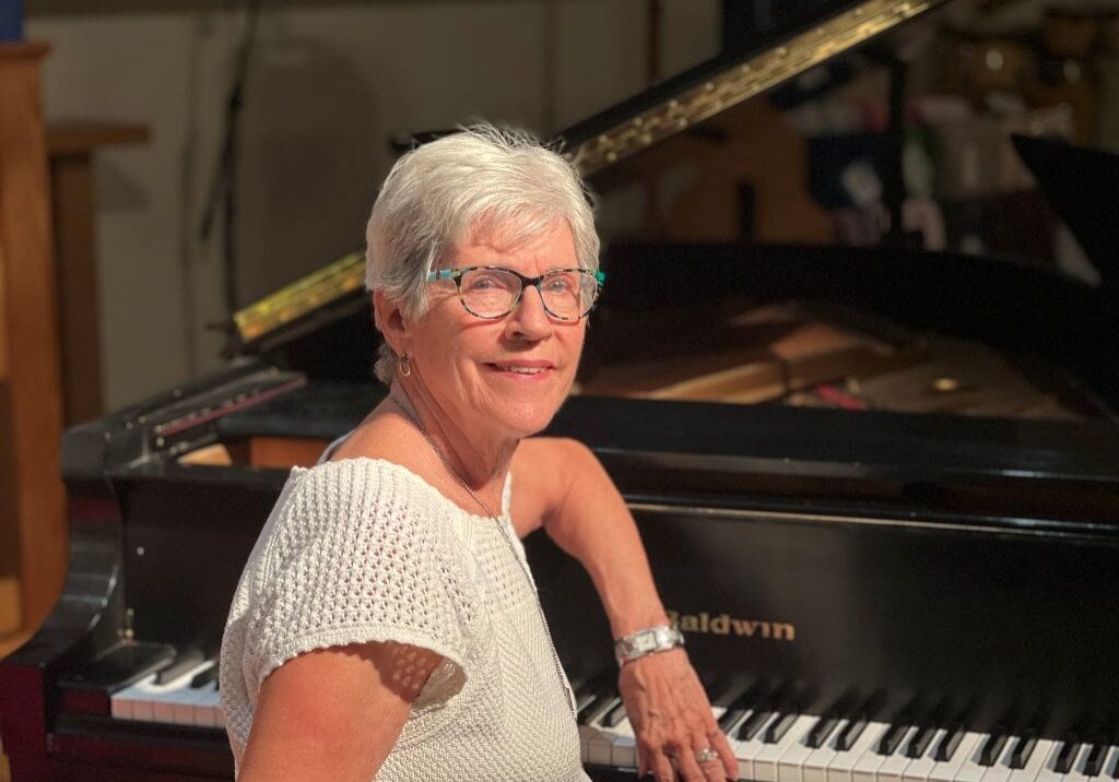 A woman standing next to a piano in front of a black grand piano.