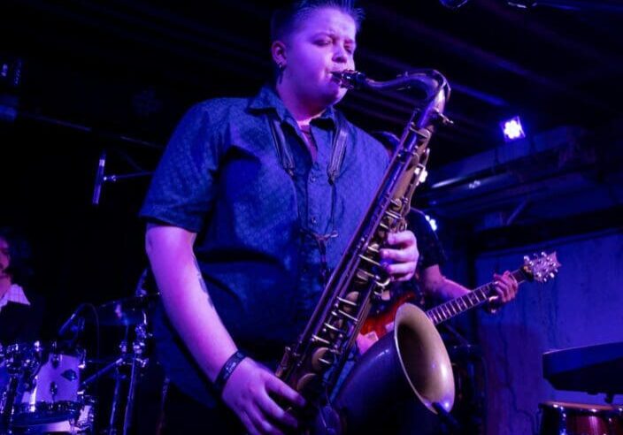 A man playing the saxophone in front of other musicians.