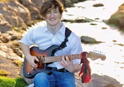 A man sitting on the grass holding a guitar.