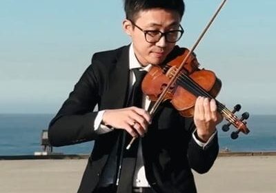 Young man playing violin outdoors with focused expression.