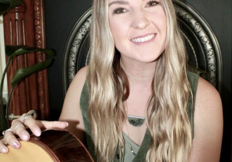 A woman holding a guitar in front of a wall.