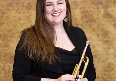 A woman holding a trumpet in front of a brown wall.